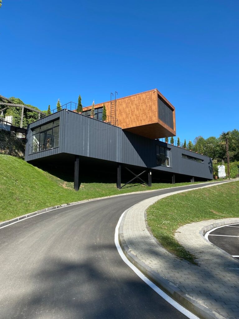 A modern elevated house with unique design featuring an overhanging structure and vibrant blue sky.